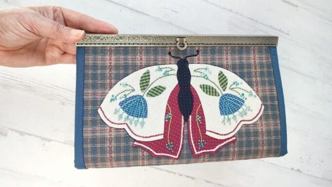 estuche con mariposa y flores aplicadas con tres bolsillos de cremallera y multibolsillos laterales, con cierre metalálico que se cose a mano.