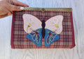 estuche con mariposa aplicada con boquilla metálica tipo cofre. Con tres bolsillos de cremallera y múltiples compartimentos.