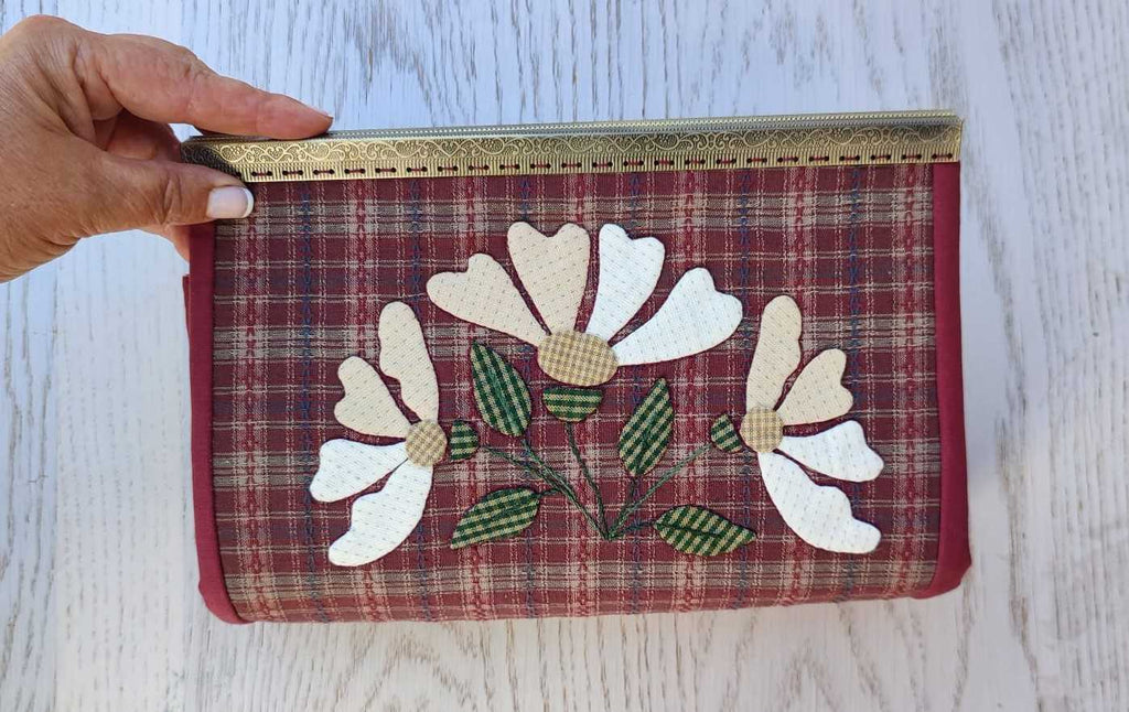 estuche con mariposa y flores aplicadas con boquilla metálica tipo cofre. Con tres bolsillos de cremallera y múltiples compartimentos.